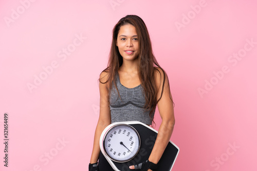 Young sport Brazilian girl over isolated pink background with weighing machine