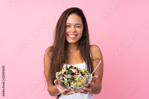 Young Brazilian girl with healthy salad over isolated pink background
