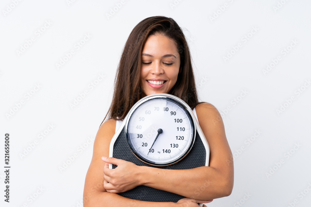 Young Brazilian girl holding a scale over isolated background with weighing machine Young Brazilian girl holding a scale over isolated background with weighing machine