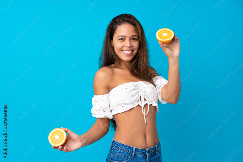 Young woman in summer holidays holding an orange over isolated blue background Young woman in summer holidays holding an orange over isolated blue background