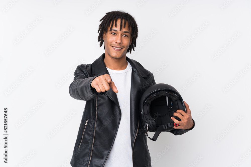 Young african american man holding a motorcycle helmet isolated on white background points finger at you with a confident expression Young african american man holding a motorcycle helmet isolated on white background points finger at you with a confident expression