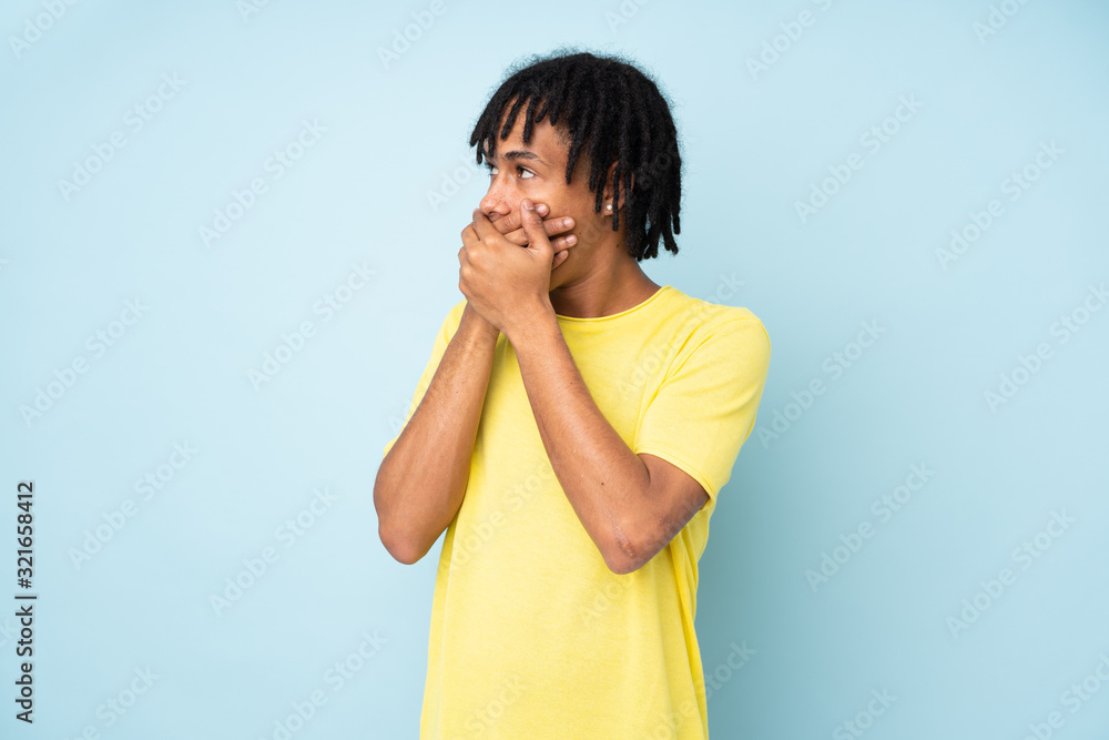 Young african american man isolated on blue background covering mouth and looking to the side