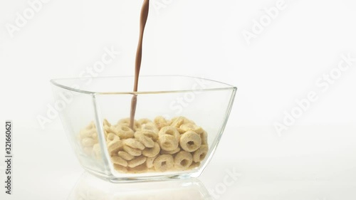 Fresh healthy food. Chocolate milk pouring into transparent bowl with yellow cereals on a white background. The concept of healthy breakfast, clean eating, dieting, vegetarian, vegan food. Side view