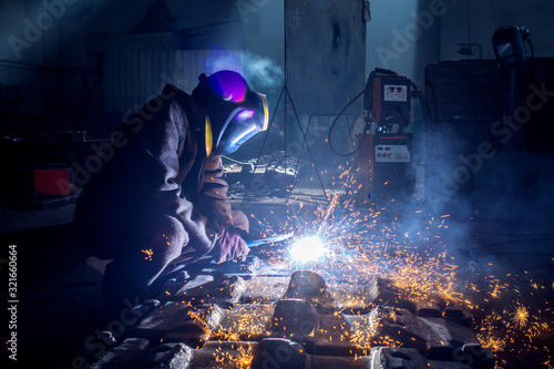 Valokuva Side view of welder in protective helmet welding metal detail with sparks at fac