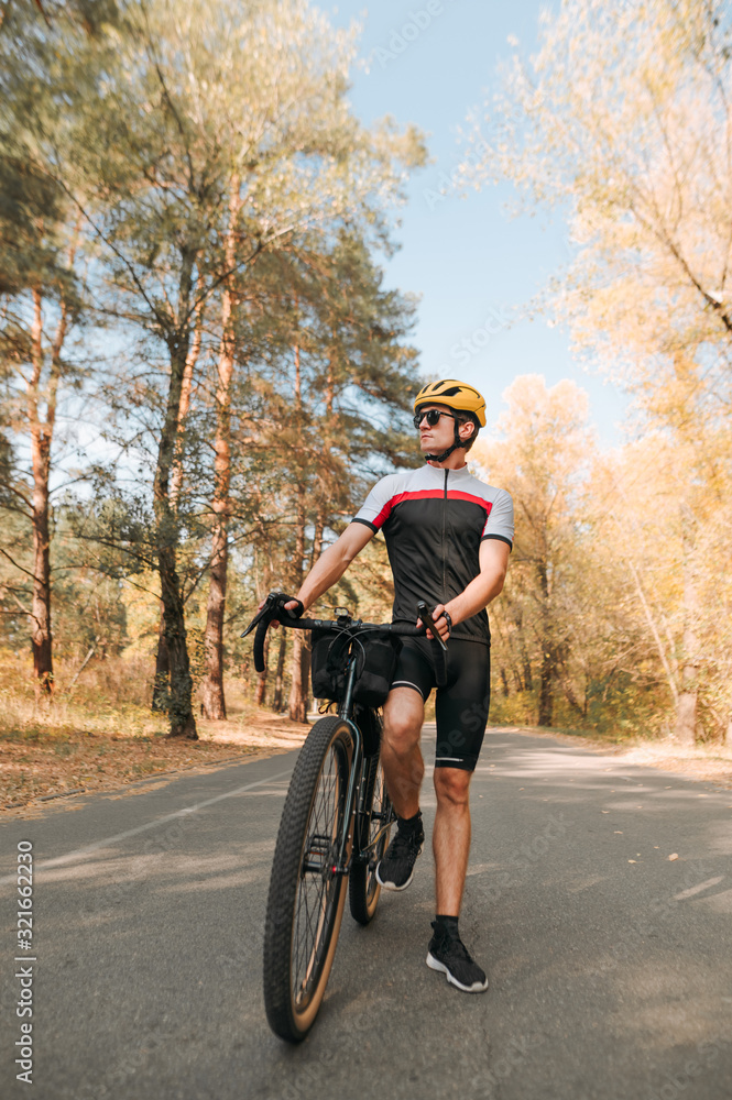 Obraz premium Portrait of a handsome man with a bicycle looking into the camera with a serious face on the background of a beautiful autumn landscape. Man posing with hiking bike in autumn forest.Vertical photo