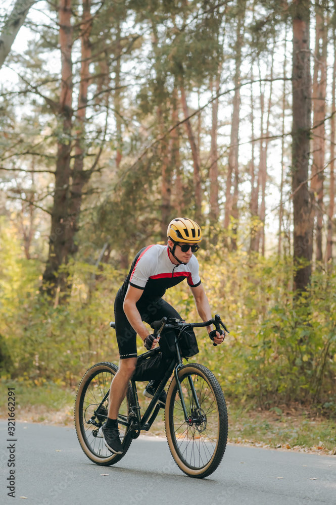 Obraz premium Portrait of a man in sports cycling clothes riding on the road in the forest and looking intently into the front. A cyclist rides a bicycle through an autumn forest. Bicycle hobby