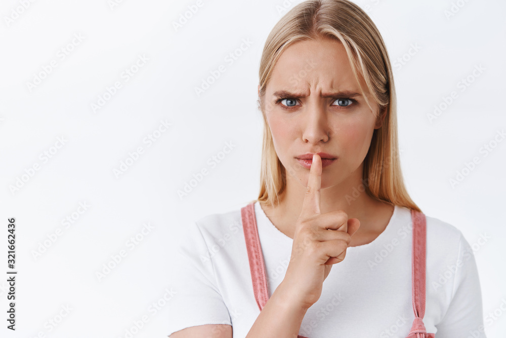 Close-up angry and furious serious-looking blond woman shushing demand silence, want you be quiet, press finger to lips to shut someone, furrow eyebrows displeased, white background Close-up angry and furious serious-looking blond woman shushing demand silence, want you be quiet, press finger to lips to shut someone, furrow eyebrows displeased, white background