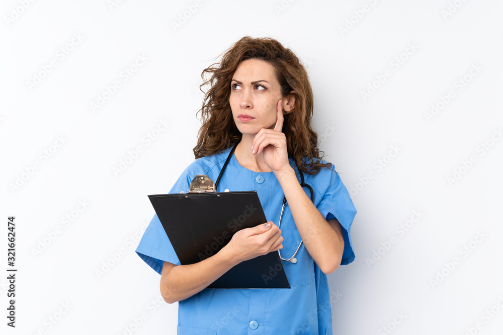 Young pretty woman over isolated background with doctor gown and holding a folder while thinking Young pretty woman over isolated background with doctor gown and holding a folder while thinking