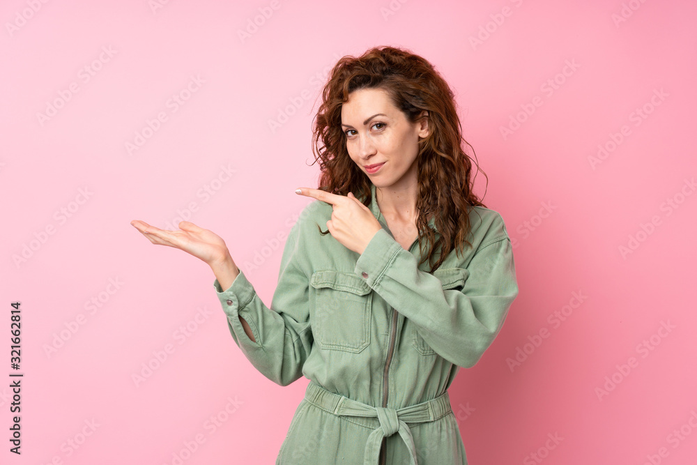 Young pretty woman over isolated pink background holding copyspace imaginary on the palm to insert an ad Young pretty woman over isolated pink background holding copyspace imaginary on the palm to insert an ad