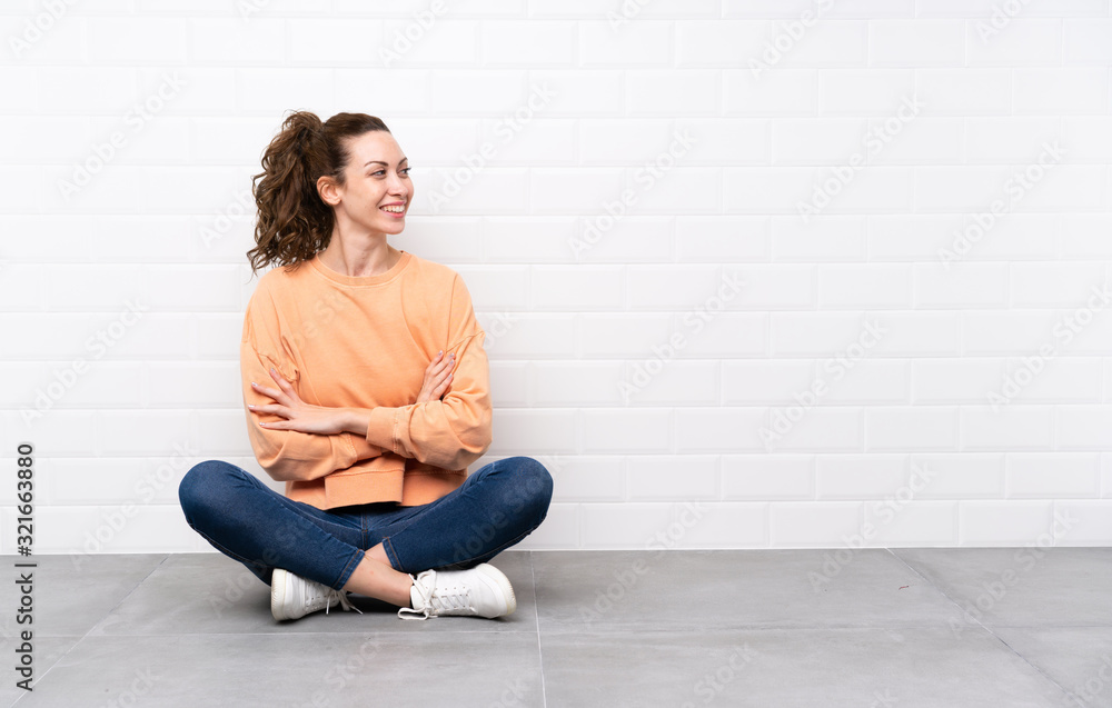 Young woman with curly hair sitting on the floor looking to the side Young woman with curly hair sitting on the floor looking to the side