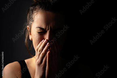 Sad grieving crying female with folded hands and tears eyes on a dark black background during trouble, life difficulties, loss and emotional problems. Copy space photo