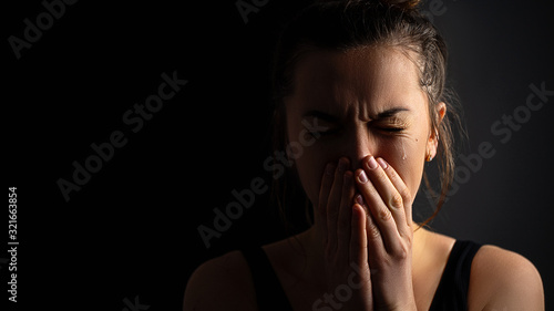 Fotografia Sad desperate grieving crying woman with folded hands and tears eyes on a dark black background during trouble, life difficulties, loss and emotional problems