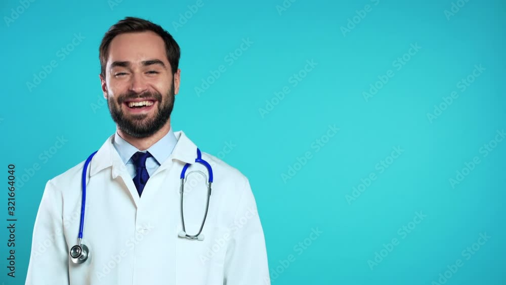 Copy space portrait of smiling man in professional medical white coat shaking head like gesture of consent and permission. Doctor isolated on blue studio background. Copy space portrait of smiling man in professional medical white coat shaking head like gesture of consent and permission. Doctor isolated on blue studio background.
