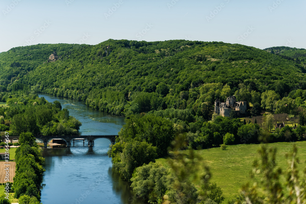 View of Dordogne river in Dordogne valley with Castelnaud-la-Chapelle Castle in right side of picture and old stone bridge in summer day. Travel tourist destination Aquitaine, France View of Dordogne river in Dordogne valley with Castelnaud-la-Chapelle Castle in right side of picture and old stone bridge in summer day. Travel tourist destination Aquitaine, France