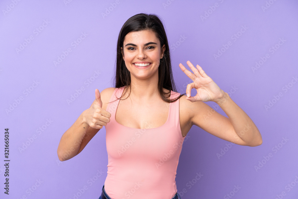Young woman over isolated purple background showing ok sign and thumb up gesture