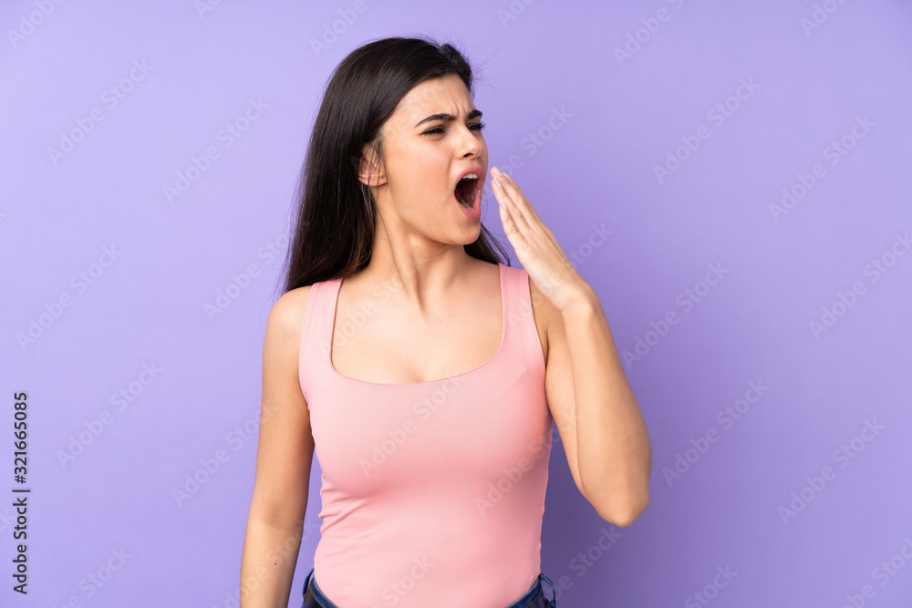 Young woman over isolated purple background yawning and covering wide open mouth with hand Young woman over isolated purple background yawning and covering wide open mouth with hand