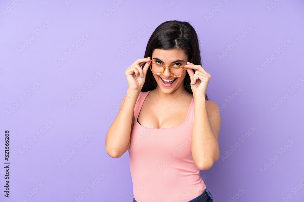 Young woman over isolated purple background with glasses and surprised