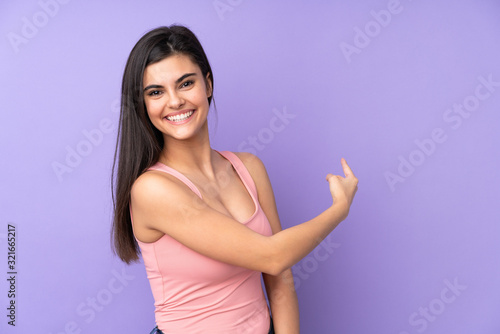 Young woman over isolated purple background pointing back