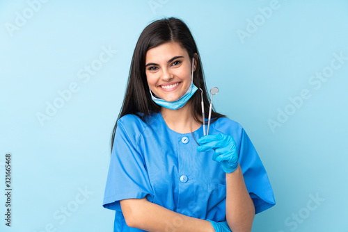 Young woman dentist holding tools over isolated blue background laughing