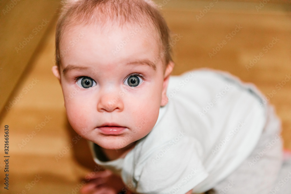 A 7-month-old baby crawls on the floor, looks down at the camera with a little fright and interest