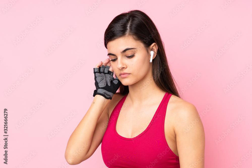 Young sport woman over isolated pink background listening music