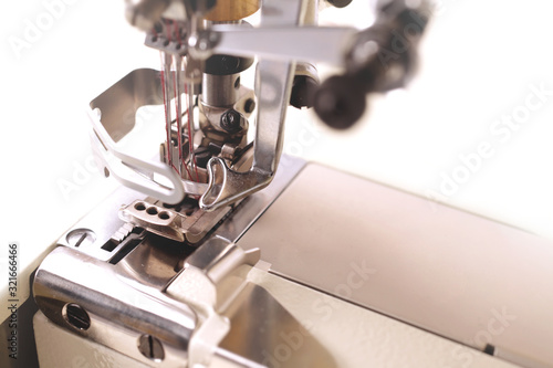 industrial coverlock sewing machine with three needles and red thread - detailled view on working area - background blanked out blurry photo