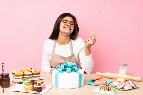 Pastry chef with a big cake in a table over isolated pink background