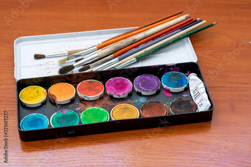  Paint brushes and watercolor paints, tempera paints on the table in a workshop, selective focus, close up