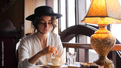 Portrait of a girl in a hat interfering with a spoon coffee at a cafe