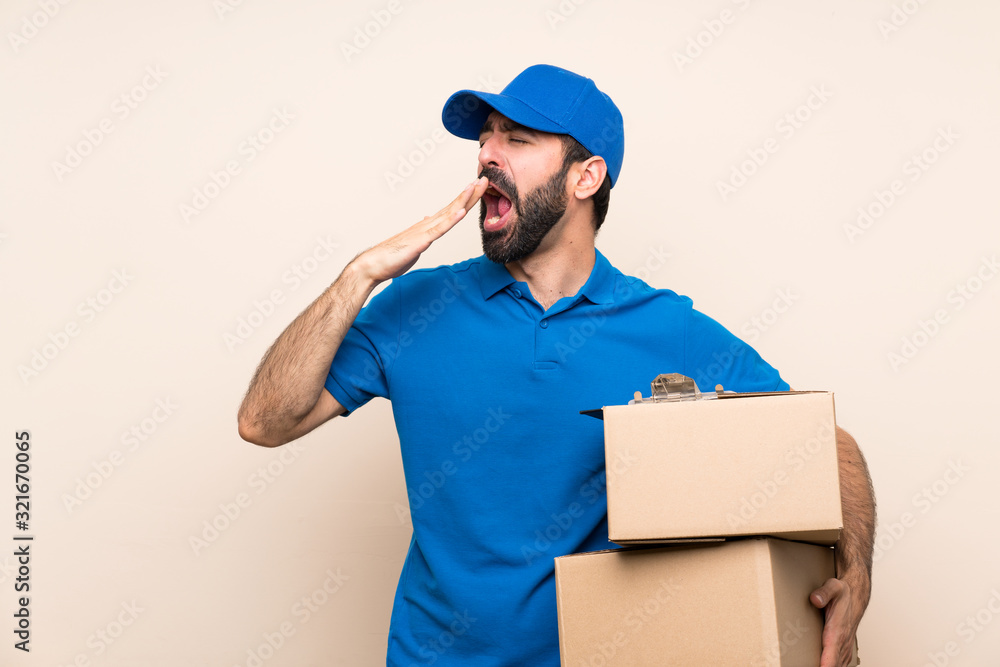 Delivery man with beard over isolated background yawning and covering wide open mouth with hand Delivery man with beard over isolated background yawning and covering wide open mouth with hand