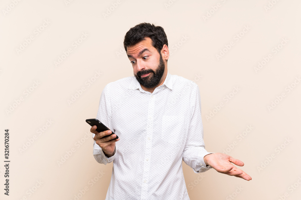 Young man with beard holding a mobile making doubts gesture Young man with beard holding a mobile making doubts gesture