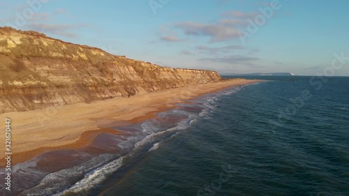 An aerial backward footage of the Hengistbury Head cliff with beautiful sandy beach and crystal blue water under a majestic blue sky and white clouds photo