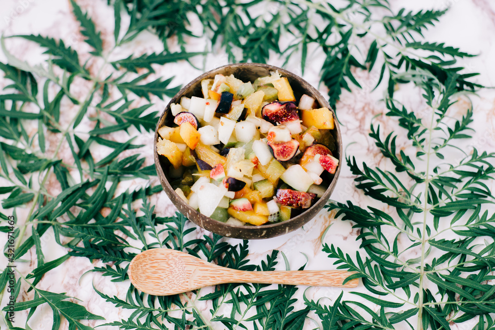 healthy fruit salad in a plate of coconut shells on the table with tropical leaves. vegetarian food healthy fruit salad in a plate of coconut shells on the table with tropical leaves. vegetarian food