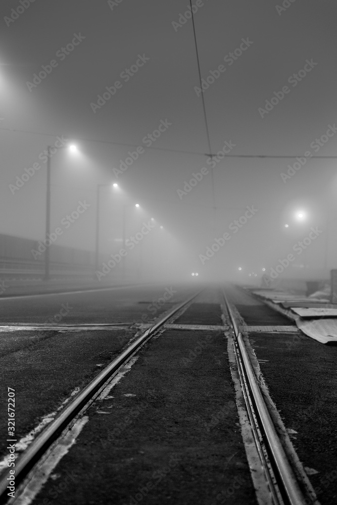 Empty road with thick fog and tram rails in foreground.