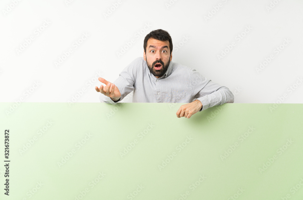 Young handsome man with beard holding a big green empty placard making doubts gesture Young handsome man with beard holding a big green empty placard making doubts gesture