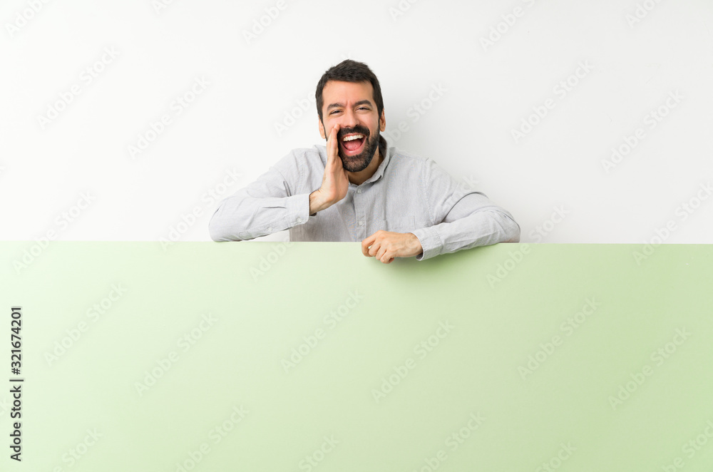 Young handsome man with beard holding a big green empty placard shouting and announcing something Young handsome man with beard holding a big green empty placard shouting and announcing something