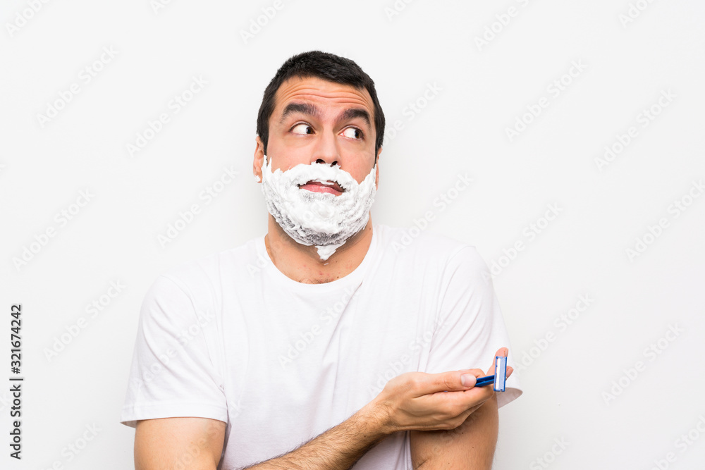 Man shaving his beard over isolated white background making doubts gesture while lifting the shoulders