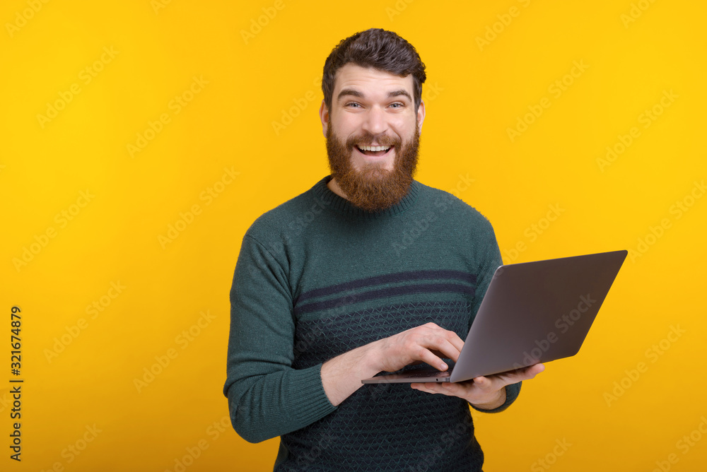 Photo of happy young man using laptop while standing over yellow background Photo of happy young man using laptop while standing over yellow background