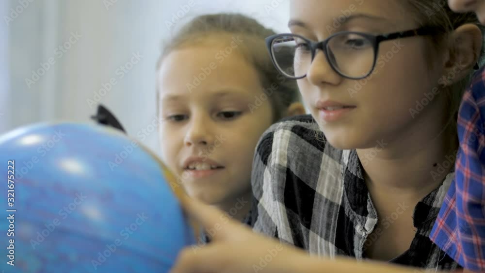 Geography lesson. Schoolmates are studying the globe on the background of a school board Geography lesson. Schoolmates are studying the globe on the background of a school board