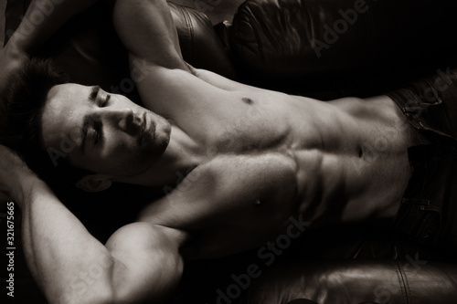 Portrait of attractive shirtless muscular man with beard and sixpack abs lying in leather armchair, sleeping.