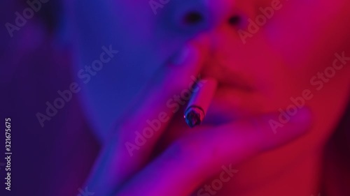 Woman lips sexually smoking cigarette focused closeup in neon lighting, slowmotion. Addicted sexy girl inhales smoke at nightclub underground party. Nightlife, alternative lifestyle concept