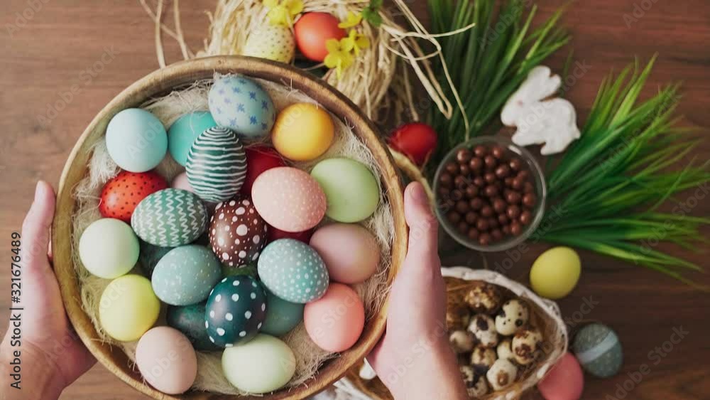 Hands holding basket full of colorful Easter eggs in front of decoration on wooden table. Easter holiday decorations, Easter concept background. Hands holding basket full of colorful Easter eggs in front of decoration on wooden table. Easter holiday decorations, Easter concept background.