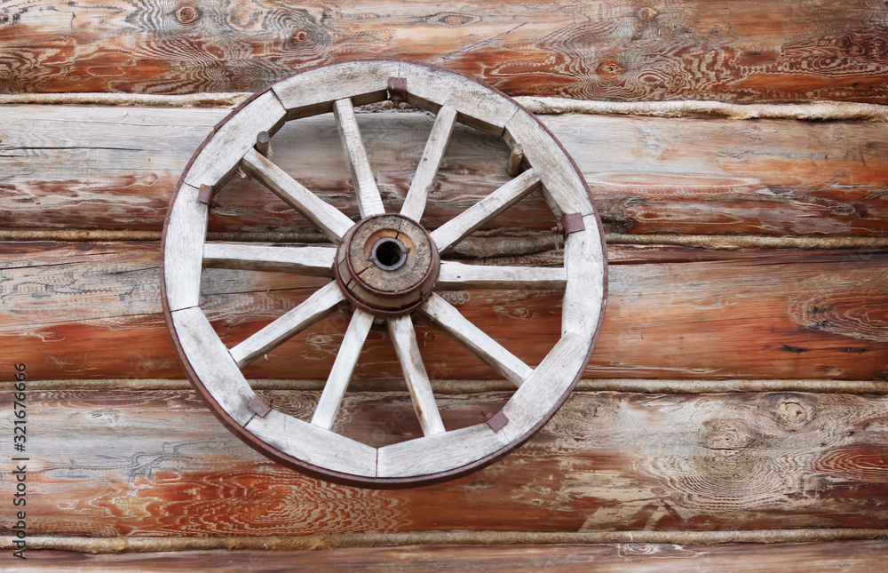 wooden wheel from a cart on the background of a wooden log house