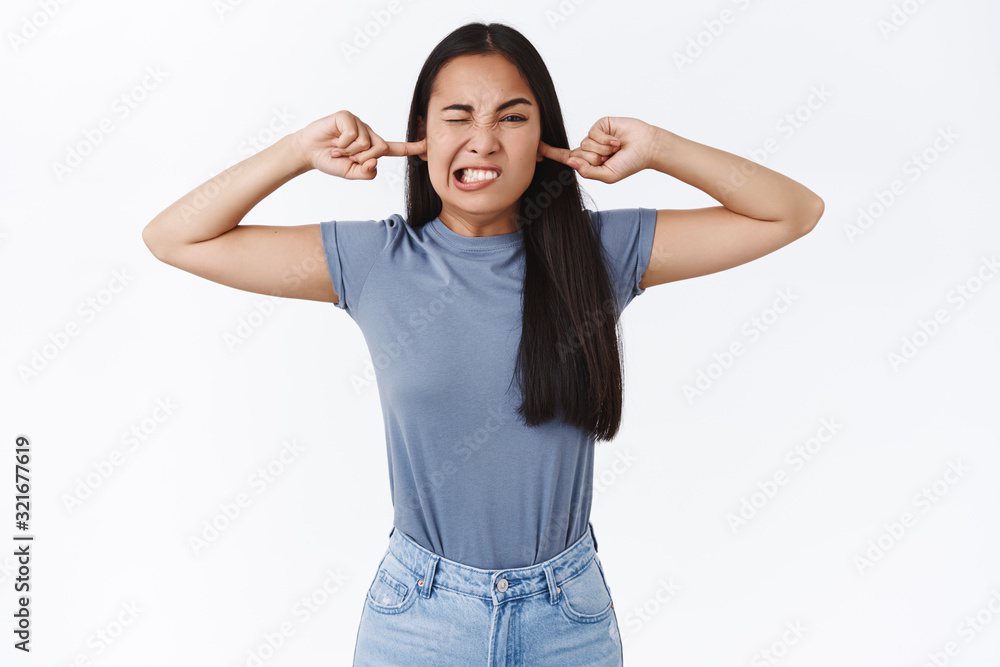 I am not hearing you. Silly and childish cute asian girl refuse listen to you as cover ears with fingers, cringe, squinting and clench teeth from bothering, disturbing loud noise, white background I am not hearing you. Silly and childish cute asian girl refuse listen to you as cover ears with fingers, cringe, squinting and clench teeth from bothering, disturbing loud noise, white background