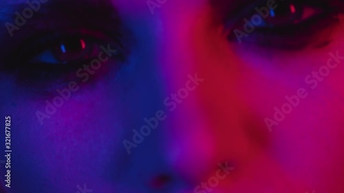 Fashion model portrait in colored neon light with dark makeup expressively looks into camera. Extreme closeup of eyes and lips. Provocative handsome girl focused shot photo
