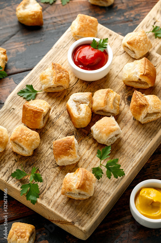 Pork sausage rolls with mustard and ketchup sauce on wooden board