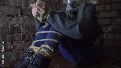 woman trying to free her hands from the rope. Sits in the basement, Close-up.