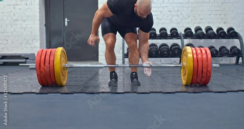 Male powerlifter lifts a very heavy weight on a barbell. Strong muscle tension in the face and body, a heavyweight raises the bar in the gym.
