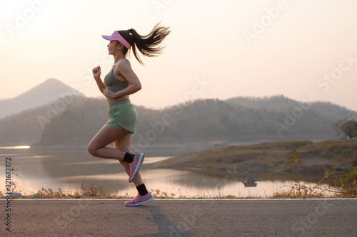 Photo side view Asia young woman runner running on asphalt road at riverside