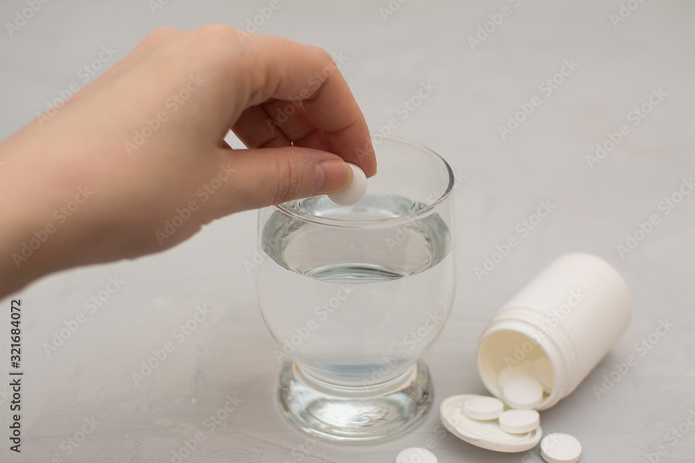 the woman put an effervescent tablet into a glass of water on a gray table. the woman put an effervescent tablet into a glass of water on a gray table.